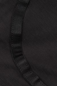 Sort stof med en glat, struktureret overflade, der har et fremtrædende satinbånd langs den ene kant. Syningen er pæn og ensartet.