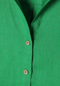 Groene linnen shirt met een uitgesneden kraag, houten knoopsluiting en een gestructureerde stof met een licht gekreukt uiterlijk.