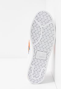 Bílá gumová podrážka tenisek s texturovaným vzorem. Obsahuje oranžové a modré akcenty. Logo 'ALL STAR CONVERSE' na obdélníkové nášivce.