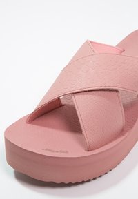 Sandale à glissière rose avec design à bande croisée, dessus texturé et semelle épaisse et lisse. Présente un motif subtil sur la surface du matériau.