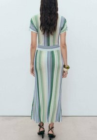 Abito maxi a righe con linee verticali in verde, blu e beige. Maniche corte, vita aderente e parte inferiore svasata. Sandali neri con strap.
