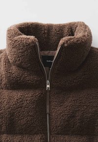 Braune Fleecejacke mit hohem Kragen, durchgehendem Reißverschluss und strukturierter Oberfläche. Markenlabel innen sichtbar. Weicher und warmer Look.