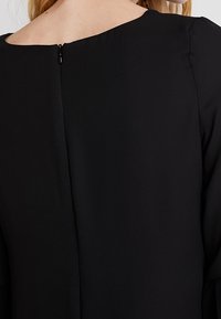 Gros plan sur le dos d’une femme portant une robe noire avec une fermeture éclair centrée dans le dos et un col rond.