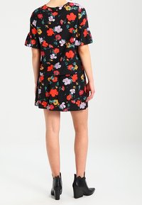 Vestido floral, fondo negro, mangas cortas con volantes, flores rojas y moradas, falda en capas, combinado con botas negras hasta el tobillo.