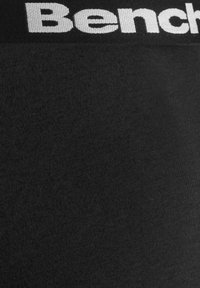 Black fitted leggings with a ribbed texture, featuring a contrasting white elastic waistband displaying the brand name "Bench."