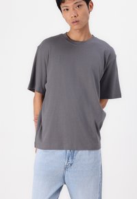 Tricou gri cu mâneci scurte, fabricat dintr-un material moale, cu o croială lejeră și gât rotund. Asortat cu blugi din denim de culoare albastră deschisă.