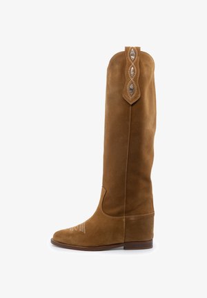 Botte de cowboy haute en daim marron avec coutures décoratives sur la pointe et une lanière de traction, talon en bois empilé bas, vue de côté sur fond blanc.