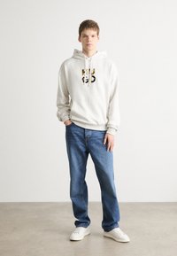 Sudadera blanca con un diseño gráfico en el pecho, combinada con jeans rectos azules y zapatillas blancas. Outfit minimalista y casual.