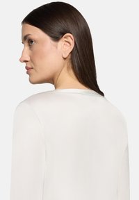 Hvid bluse med enkelt design, rund halsudskæring og lange ærmer. Stoffet virker glat og let. Set bagfra.