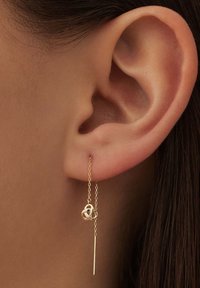 Boucles d'oreilles en fil d'or présentant un nœud décoratif et un design en tige droite, suspendues à une chaîne délicate. Texture lisse, finition raffinée.