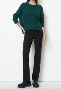 Pull en maille texturée couleur bleu sarcelle avec poignets et ourlet côtelés, associé à un jean noir ajusté et des chaussures noires épaisses. Design simple, sans motifs visibles.