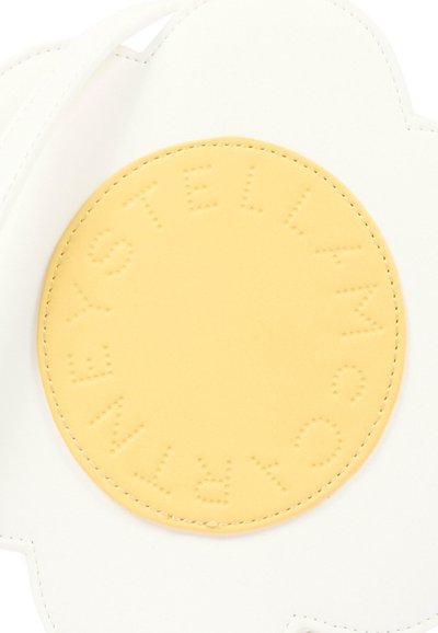 Biała torebka w kształcie kwiatu z dużą żółtą okrągłą naszywką z wypukłym napisem „STELLA MCCARTNEY” tworzącym pierścień wokół środka.