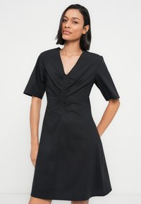 Μαύρο φόρεμα με V λαιμόκοψη, κοντά μανίκια, ραμμένο με πιέτες στο μπροστινό μέρος και φούστα με φαρδιά γραμμή. Κατασκευασμένο από απαλό ύφασμα με ματ όψη.