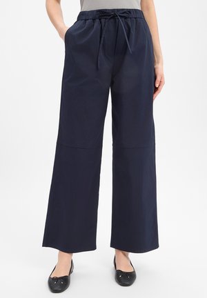 Navy blue wide-leg pants with elastic waistband and drawstring, worn with black ballet flats and light gray top.