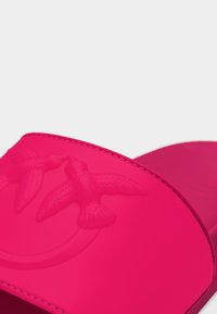 Φωτεινό ροζ σανδάλι με σχέδιο ανάγλυφων δύο πουλιών που αγγίζουν τις ράμφες τους στο λουράκι, εμφανίζεται σε απλό φόντο.