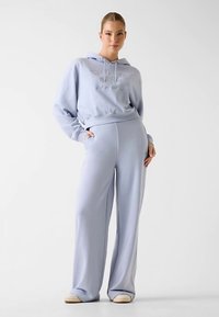 Ensemble sweat à capuche et pantalon assortis bleu clair, en tissu doux. Le sweat à capuche arbore un logo sur le devant, et le pantalon a une coupe décontractée.