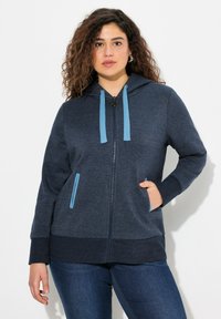 Felpa con zip di colore blu navy in morbido tessuto, dotata di cappuccio, lacci blu e due tasche laterali con dettagli blu. Polsini e orlo a coste.