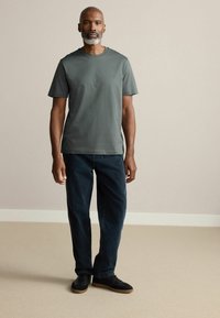 Tricou gri cu mâneci scurte, cu guler rotund, purtat alături de blugi negri și adidași negri. Material moale și neted, cu o croială regulară.