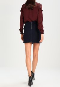 Blusa bordeaux con maniche a volant e dettagli in pizzo, abbinata a una minigonna di jeans scuro. Stivaletti neri completano l'outfit.