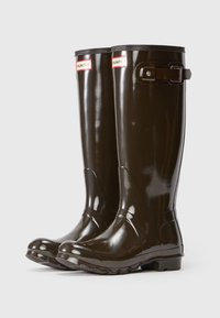 Botas altas de goma marrones con un acabado brillante, que cuentan con un hebilla lateral ajustable y una suela texturizada para mayor agarre. Etiqueta de la marca en la parte frontal.