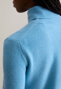 Light blue ribbed turtleneck sweater with a fitted design, featuring a mock neck and seamless shoulder detailing, made of soft textured material.