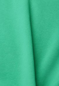 Tissu vert lisse avec un pli vertical subtil créant une ombre douce au centre.
