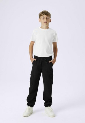 Witte katoenen T-shirt, zwarte cargobroek met zijzakken en witte sneakers. De outfit heeft een relaxte pasvorm en een elastische tailleband.
