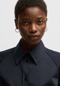 Dark navy shirt with a pointed collar, button placket, and raglan sleeves. Smooth fabric texture with subtle stitching details.