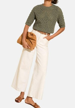 Vrouw draagt een olijfgroen gehaakt kortärmelig topje, witte broek met wijde pijpen en hoge taille, bruine riem en beige sandalen, en houdt een grote bruine clutch vast.