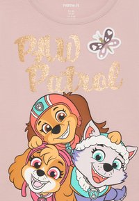 Svijetlo ružičasta pamučna majica s tri crtana psa s nasmijanim licima, sjajni zlatni natpis "PAW Patrol" i aplikacija leptira.