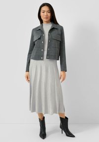 Grau gekürzte Jacke mit zwei Brusttaschen, kombiniert mit einem langen silbernen Kleid. Schwarze spitze Stiefeletten vervollständigen das Outfit.