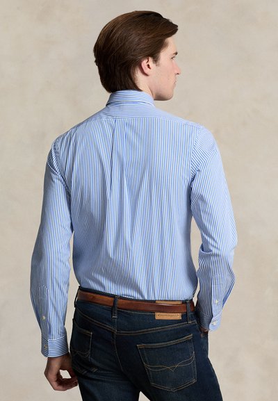 Svetlomodrá a bielo pruhovaná košeľa s gombíkmi na golieri, dlhými rukávmi a tmavomodré rifle s hnedým koženým opaskom a detailmi.