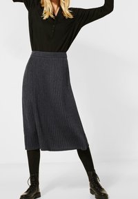 Jupe midi côtelée gris foncé avec une taille ajustée, associée à un haut noir à manches longues et boutons et des bottes de combat noires à lacets.