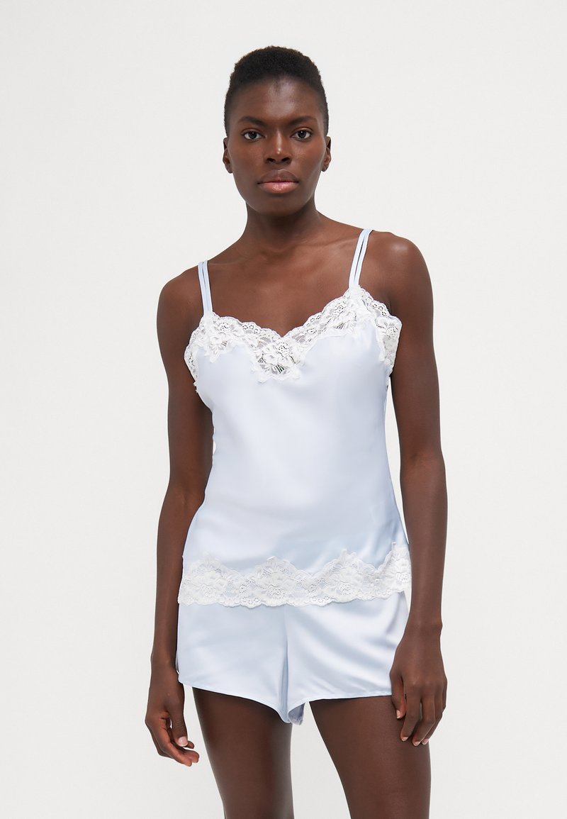 Vaaleansiniset satiinipyjamat, joissa on pitsireunus. Setti sisältää säätöhirveillä varustetun toppimaisen paidan ja siihen sopivat shortsit. Silkkinen pinta, hersyvä muotoilu.