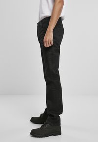 Crne traperice ravnog kroja, s klasičnim dizajnom od pet džepova i metalnim detaljima, uparenim s crnim čizmama na vezivanje.