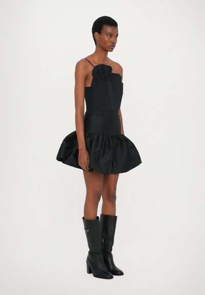 Vestido negro sin tirantes con un frente plisado, dobladillo rizado y textura suave. Combinado con botas de cuero negro hasta la rodilla.