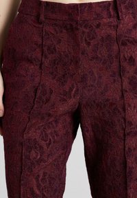 Pantalones de encaje burdeos con un patrón floral, superficie texturizada y una cinturilla elegante con pliegues frontales para un aspecto entallado.