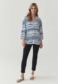Bluză cu mâneci lungi și decolteu în V, de culoare albă, cu dungi orizontale albastre și bleumarin. Asortată cu pantaloni închisi la culoare și sandale deschise. Textură moale, croială lejeră.