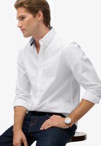 Witte katoenen shirt met een button-down kraag, met een contrasterende zwarte accenten. Draagt het met donkerblauwe jeans en een horloge.