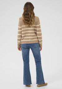 Brūns un krēmkrāsas svītrains džemperis ar garām piedurknēm, saskaņots ar ziliem platākiem džinsiem un bēšām kurpēm, skatīts no aizmugures.