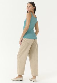 Débardeur côtelé en teal avec un col en rond, associé à un pantalon large beige et des ballerines de couleur claire. Design minimaliste, texture douce.
