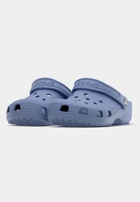 Μπλε καουτσούκ σαμπό με αεριζόμενες τρύπες και λουρί πίσω, διαθέτοντας υφασμάτινες σόλες και το όνομα της μάρκας ανάγλυφο στο πλάι.