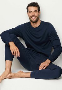 Sada domácího oblečení v námořnické modři vyrobená z měkké tkaniny. Obsahuje mikinu s kulatým výstřihem a úzké kalhoty s elastickými manžetami a hladkou texturou.