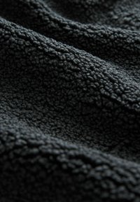 Tissu polaire noir doux avec une surface texturée et bouclée, présenté en gros plan avec plis et ombres.
