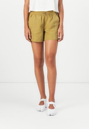 Shorts kaki en tissu léger, dotés d'une taille élastique, de poches latérales et de coutures contrastées. Portés avec des chaussures blanches.