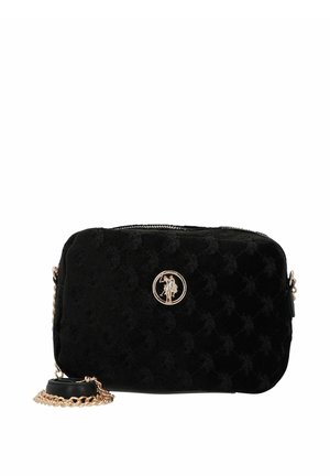 Bolso bandolera de terciopelo negro con diseño acolchado, herrajes dorados y un logo circular en la parte frontal. Incluye una correa de cadena.