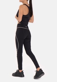 Must värviline treeningkomplekt, mis koosneb tihedast tank-topist ja kõrge vöökohaga retuusidest, valgete lisaniididetailidega, koos mustade jooksusapikutega.