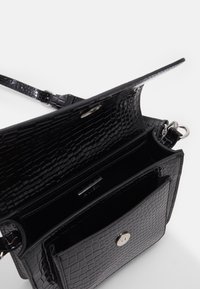 Černá kabelka z texturovaného, lesklého materiálu s krokodýlím vzorem. Má stříbrné zapínání na cvoček a nastavitelný popruh.