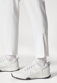 Λευκά αθλητικά παντελόνια με φερμουάρ στους αστραγάλους, συνδυασμένα με λευκά αθλητικά παπούτσια που έχουν υφή και αντίθετους σκούρους σόλες.