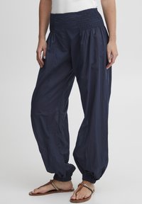 Pantalones ligeros de color azul marino con una cintura fruncida, corte holgado y puños fruncidos, confeccionados en una tela lisa y transpirable.